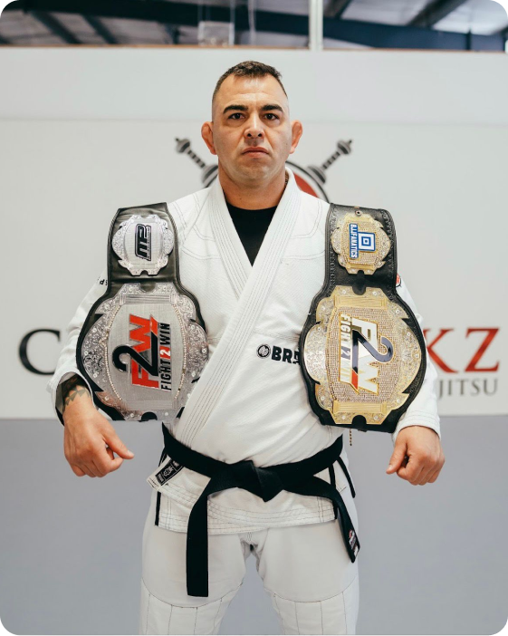 Portrait of Professor Alexandro Ceconi, Brazilian Jiu-Jitsu instructor at Ceconi BJJ Cypress. Alexandro Ceconi wearing a white gi and black belt with championship belts