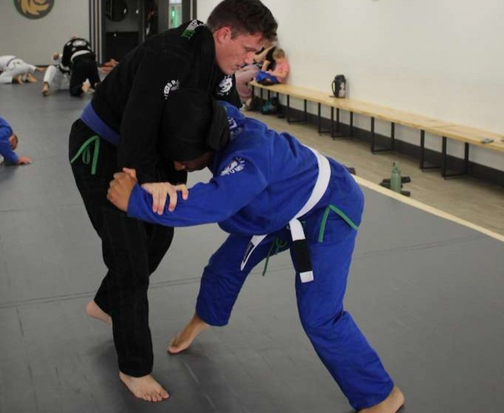 Training partners drilling a takedown during a Jiu-Jitsu class at Ceconi BJJ Cypress. Students in black and blue gis practicing a standing Brazilian Jiu-Jitsu technique at Ceconi BJJ Cypress