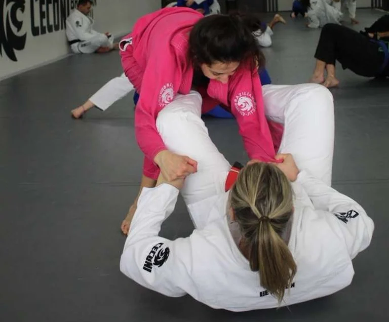Training partners practicing a ground position in the women-only Jiu-Jitsu program. Women practicing Brazilian Jiu-Jitsu in pink and white gis